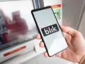 Dłoń trzyma smartfon z logo Blik. Obok bankomat, ale blik nie doszedł.