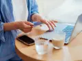 Kobieta dokonuje płatności kartą w internecie, wpisując dane na laptopie. Obok leży telefon i napoje.