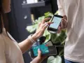 Kobieta wpisuje PIN na telefonie, który służy jako terminal płatniczy. Obok trzyma kartę Visa.