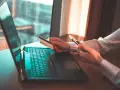 Osoba z kartą płatniczą i telefonem przy laptopie, szuka informacji jak cofnąć przelew Santander.