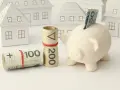 Świnka-skarbonka z banknotami i zwinięte pieniądze na tle domków. Czy kredyt konsolidacyjny się opłaca?