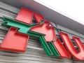Neonowy napis Auchan, przypominający skarbonkę, z charakterystycznym zielonym ptaszkiem.