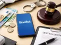 Telefon z logo Revolut, banknoty, monety, kajdanki i dokument "Debt Collection" sugerują problemy z długami i interwencję komornika.