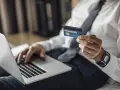 Mężczyzna w koszuli i krawacie trzyma kartę Visa Silver, gotowy do płatności online. Akcja pajacyk w tle.