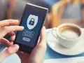 Dłoń trzyma smartfon z ekranem logowania do banku. Widoczny symbol tarczy z kłódką, pola na login i hasło.