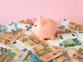 Różowa świnka-skarbonka na stosie banknotów euro. Zastanawiasz się nad oprocentowaniem konta walutowego?