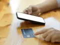 Dłoń trzyma smartfon, obok leży karta kredytowa. Szybkie zakupy online, jak w millennium impresja sklepy.