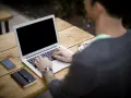 Mężczyzna pracuje na laptopie przy stoliku na zewnątrz. Obok leży telefon, notatnik i kawa. Może właśnie zarabia na **moneyo.pl**.