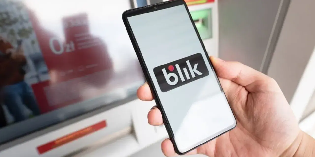 Dłoń trzyma smartfon z logo Blik. Obok bankomat, ale blik nie doszedł.