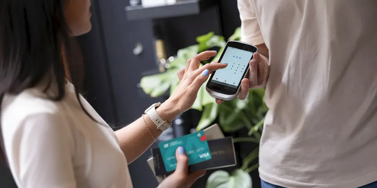 Kobieta wpisuje PIN na telefonie, który służy jako terminal płatniczy. Obok trzyma kartę Visa.