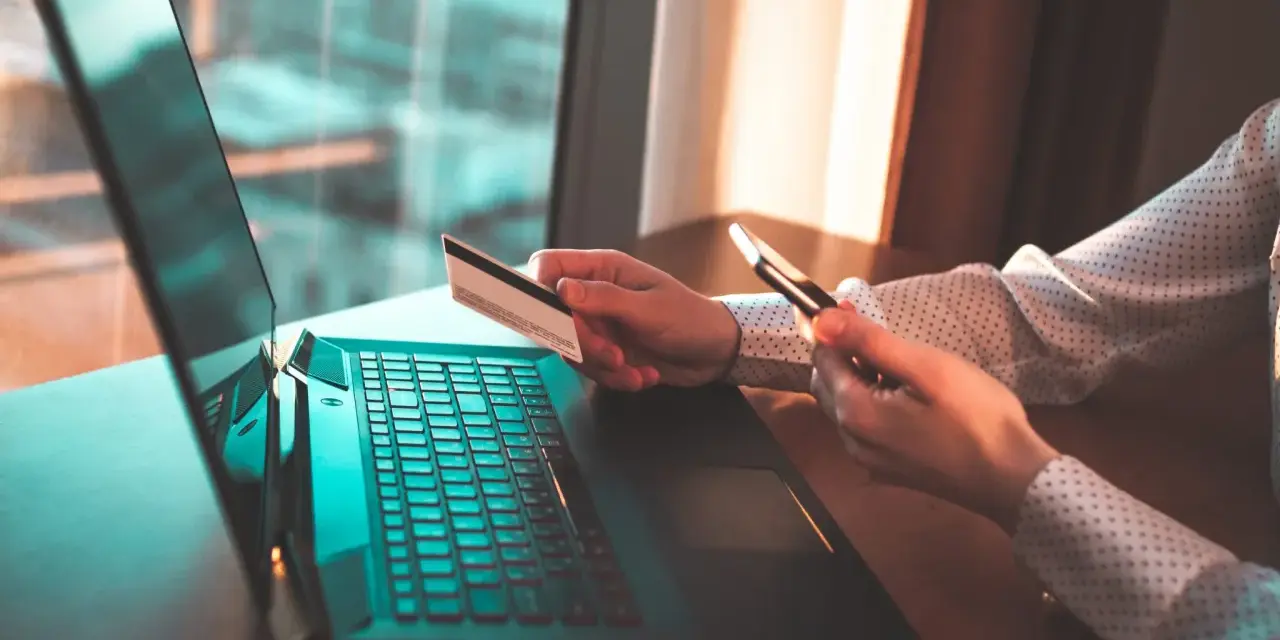 Osoba z kartą płatniczą i telefonem przy laptopie, szuka informacji jak cofnąć przelew Santander.