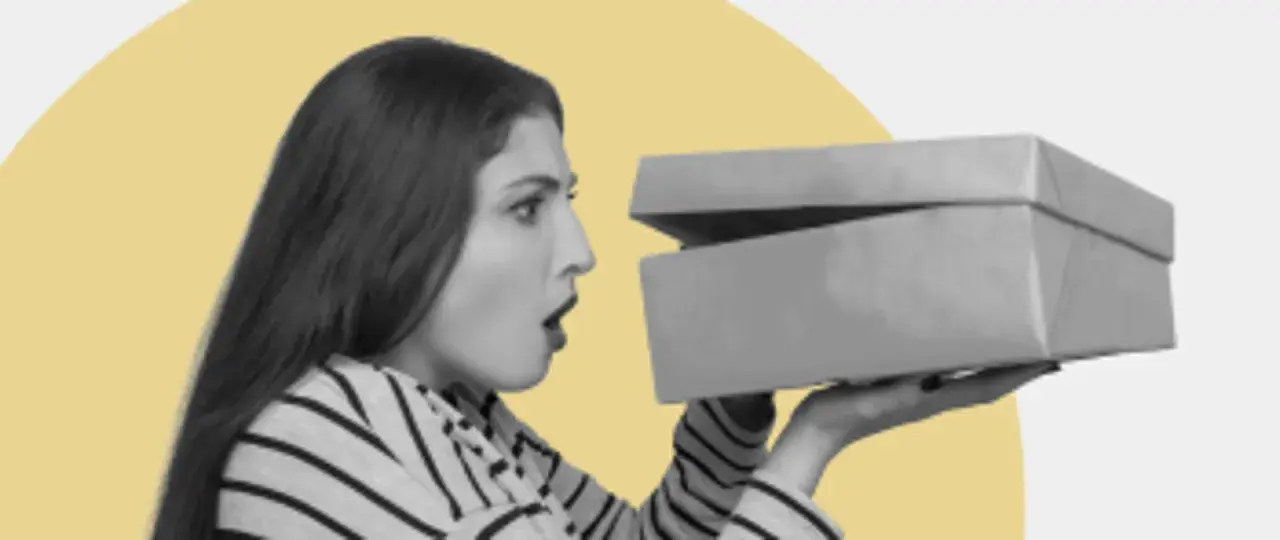 Zaskoczona kobieta otwiera pudełko z zakupami. Czy to prezent? GFK moje zakupy.