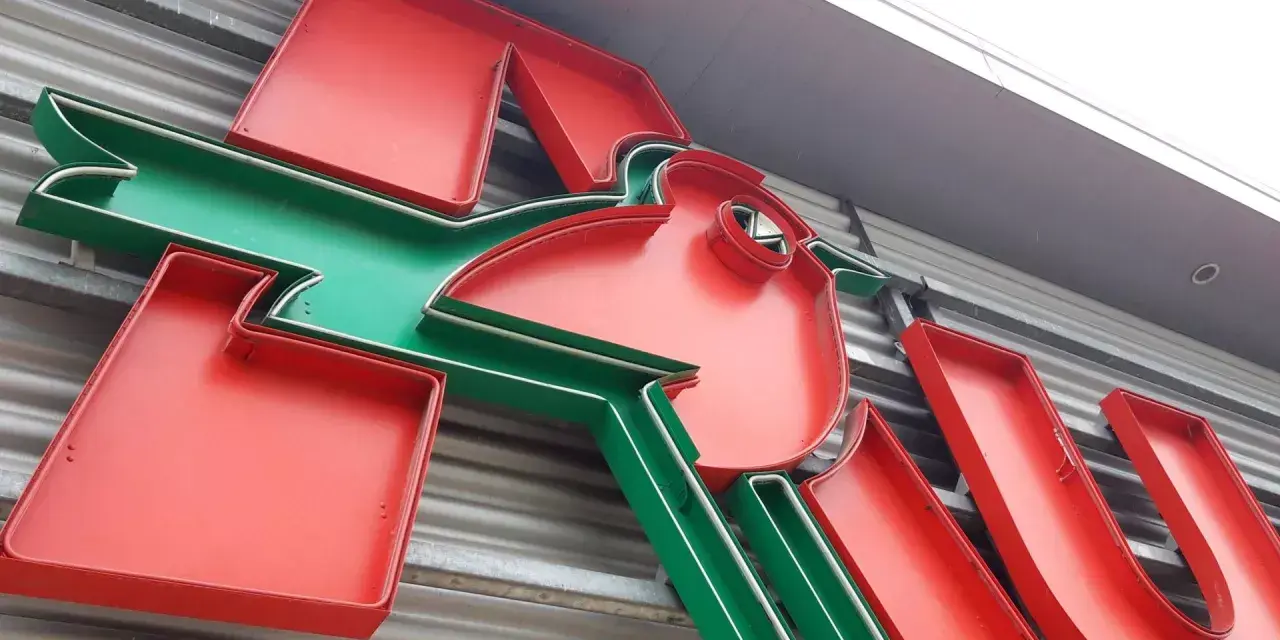 Neonowy napis Auchan, przypominający skarbonkę, z charakterystycznym zielonym ptaszkiem.