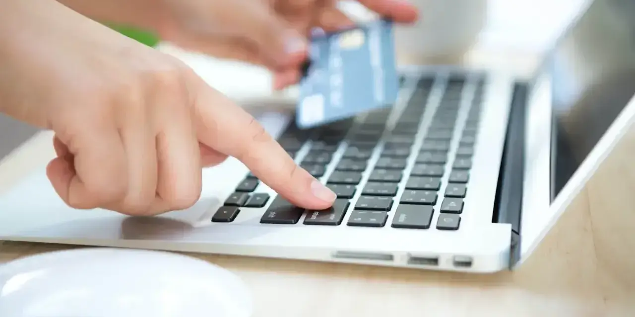 Dłonie wprowadzają dane karty na laptopie, zastanawiając się, czy Skrill jest bezpieczny.