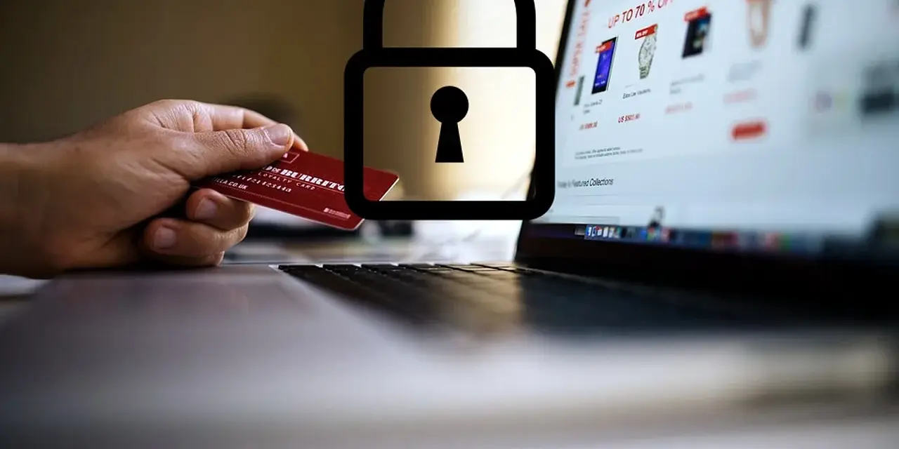 Dłoń trzyma kartę debetową przy laptopie z otwartą stroną sklepu internetowego. Symbol kłódki nad kartą sugeruje, czy kartą debetową można płacić w internecie bezpiecznie.