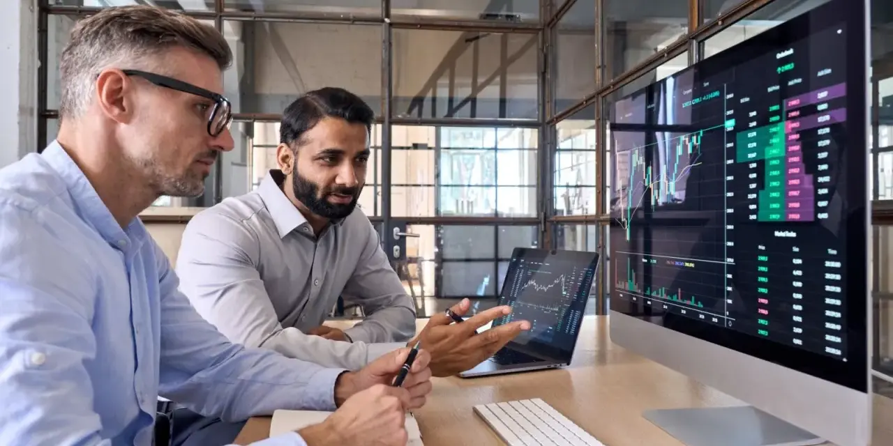 Dwóch mężczyzn analizuje wykresy giełdowe, dyskutując, w co inwestować krótkoterminowo.