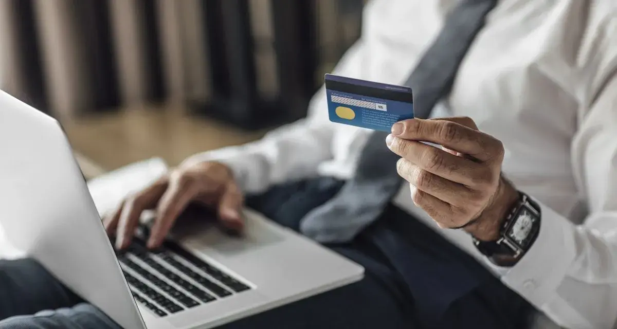 Mężczyzna w koszuli i krawacie trzyma kartę Visa Silver, gotowy do płatności online. Akcja pajacyk w tle.
