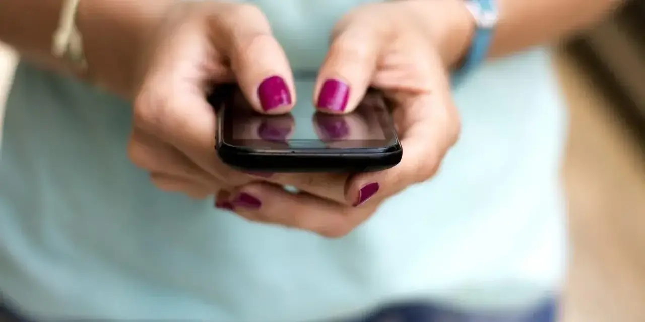 Dłonie z malowanymi paznokciami piszą na telefonie, być może ustawiając ipko zmiana limitu przelewu.