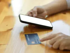 Dłoń trzyma smartfon, obok leży karta kredytowa. Szybkie zakupy online, jak w millennium impresja sklepy.