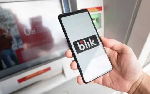 Dłoń trzyma smartfon z logo Blik. Obok bankomat, ale blik nie doszedł.