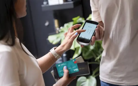 Kobieta wpisuje PIN na telefonie, który służy jako terminal płatniczy. Obok trzyma kartę Visa.