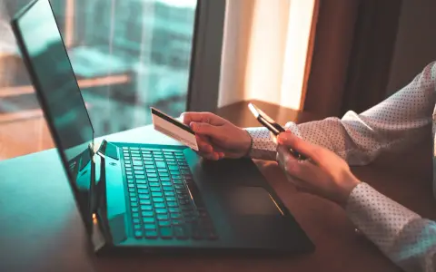 Osoba z kartą płatniczą i telefonem przy laptopie, szuka informacji jak cofnąć przelew Santander.
