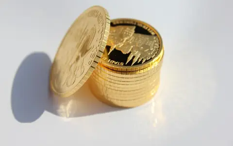 Stos złotych monet, jedna uchylona, zachęca do refleksji: czy kupować złoto? Błyszczące monety z wizerunkiem miasta budzą zainteresowanie.