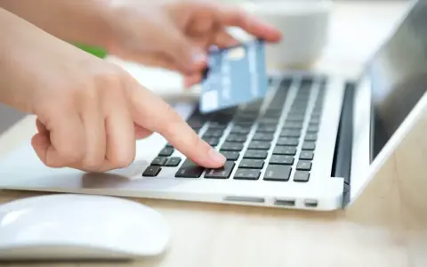 Dłonie wprowadzają dane karty na laptopie, zastanawiając się, czy Skrill jest bezpieczny.