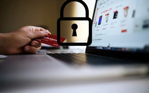Dłoń trzyma kartę debetową przy laptopie z otwartą stroną sklepu internetowego. Symbol kłódki nad kartą sugeruje, czy kartą debetową można płacić w internecie bezpiecznie.