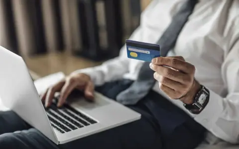 Mężczyzna w koszuli i krawacie trzyma kartę Visa Silver, gotowy do płatności online. Akcja pajacyk w tle.