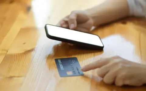 Dłoń trzyma smartfon, obok leży karta kredytowa. Szybkie zakupy online, jak w millennium impresja sklepy.