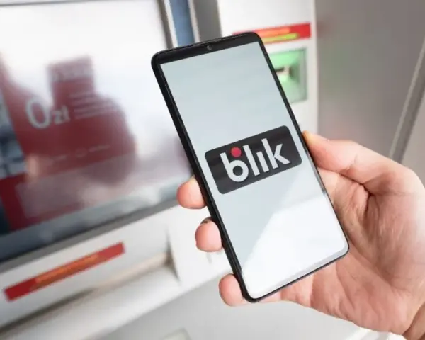 Dłoń trzyma smartfon z logo Blik. Obok bankomat, ale blik nie doszedł.