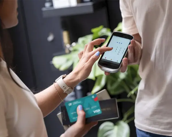 Kobieta wpisuje PIN na telefonie, który służy jako terminal płatniczy. Obok trzyma kartę Visa.