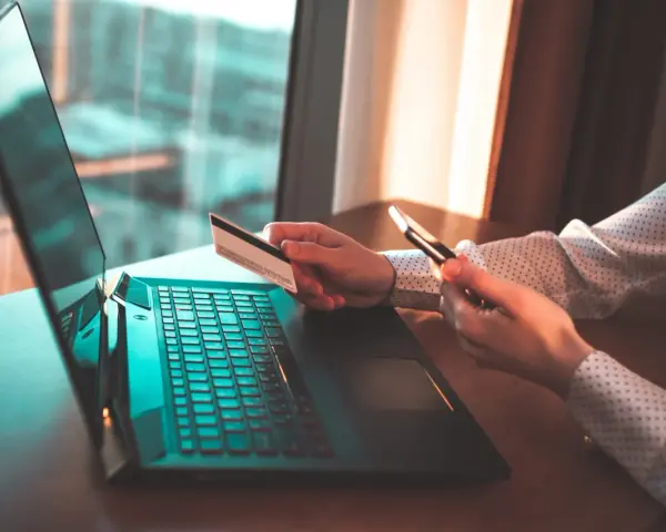 Osoba z kartą płatniczą i telefonem przy laptopie, szuka informacji jak cofnąć przelew Santander.