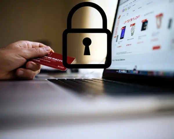 Dłoń trzyma kartę debetową przy laptopie z otwartą stroną sklepu internetowego. Symbol kłódki nad kartą sugeruje, czy kartą debetową można płacić w internecie bezpiecznie.
