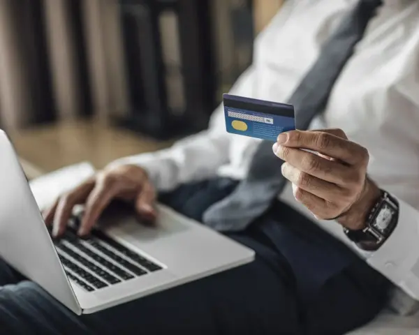 Mężczyzna w koszuli i krawacie trzyma kartę Visa Silver, gotowy do płatności online. Akcja pajacyk w tle.