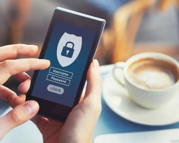 Dłoń trzyma smartfon z ekranem logowania do banku. Widoczny symbol tarczy z kłódką, pola na login i hasło.