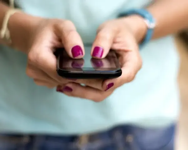 Dłonie z malowanymi paznokciami piszą na telefonie, być może ustawiając ipko zmiana limitu przelewu.