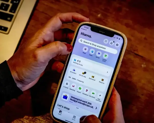 Dłoń trzyma smartfon z aplikacją Klarna. Czy Klarna jest bezpieczna? Aplikacja oferuje zakupy, płatności i zarządzanie zamówieniami.
