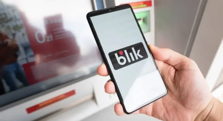 Dłoń trzyma smartfon z logo Blik. Obok bankomat, ale blik nie doszedł.