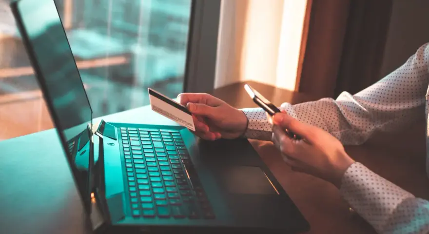 Osoba z kartą płatniczą i telefonem przy laptopie, szuka informacji jak cofnąć przelew Santander.