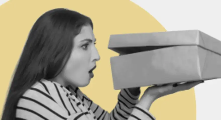 Zaskoczona kobieta otwiera pudełko z zakupami. Czy to prezent? GFK moje zakupy.