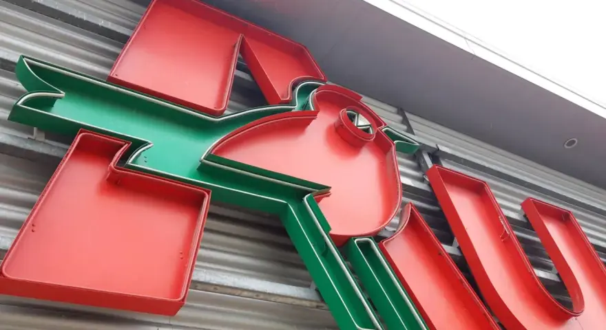 Neonowy napis Auchan, przypominający skarbonkę, z charakterystycznym zielonym ptaszkiem.
