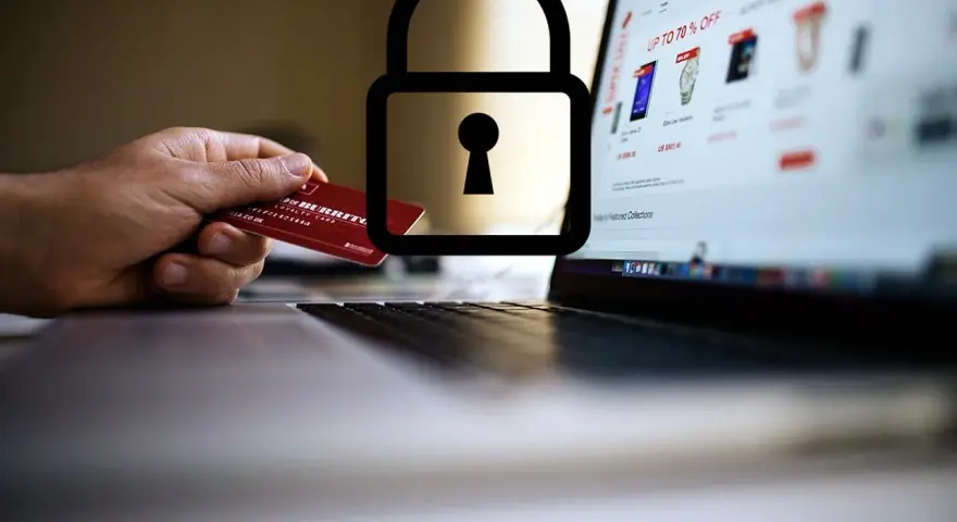 Dłoń trzyma kartę debetową przy laptopie z otwartą stroną sklepu internetowego. Symbol kłódki nad kartą sugeruje, czy kartą debetową można płacić w internecie bezpiecznie.