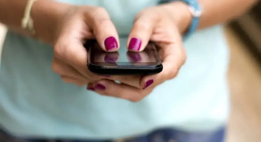 Dłonie z malowanymi paznokciami piszą na telefonie, być może ustawiając ipko zmiana limitu przelewu.