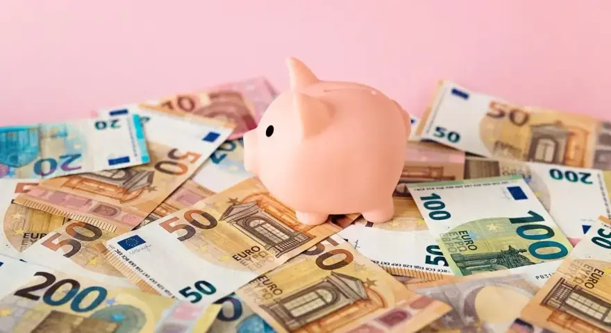 Różowa świnka-skarbonka na stosie banknotów euro. Zastanawiasz się nad oprocentowaniem konta walutowego?