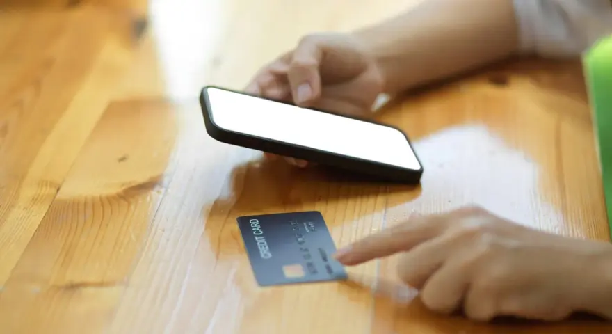 Dłoń trzyma smartfon, obok leży karta kredytowa. Szybkie zakupy online, jak w millennium impresja sklepy.