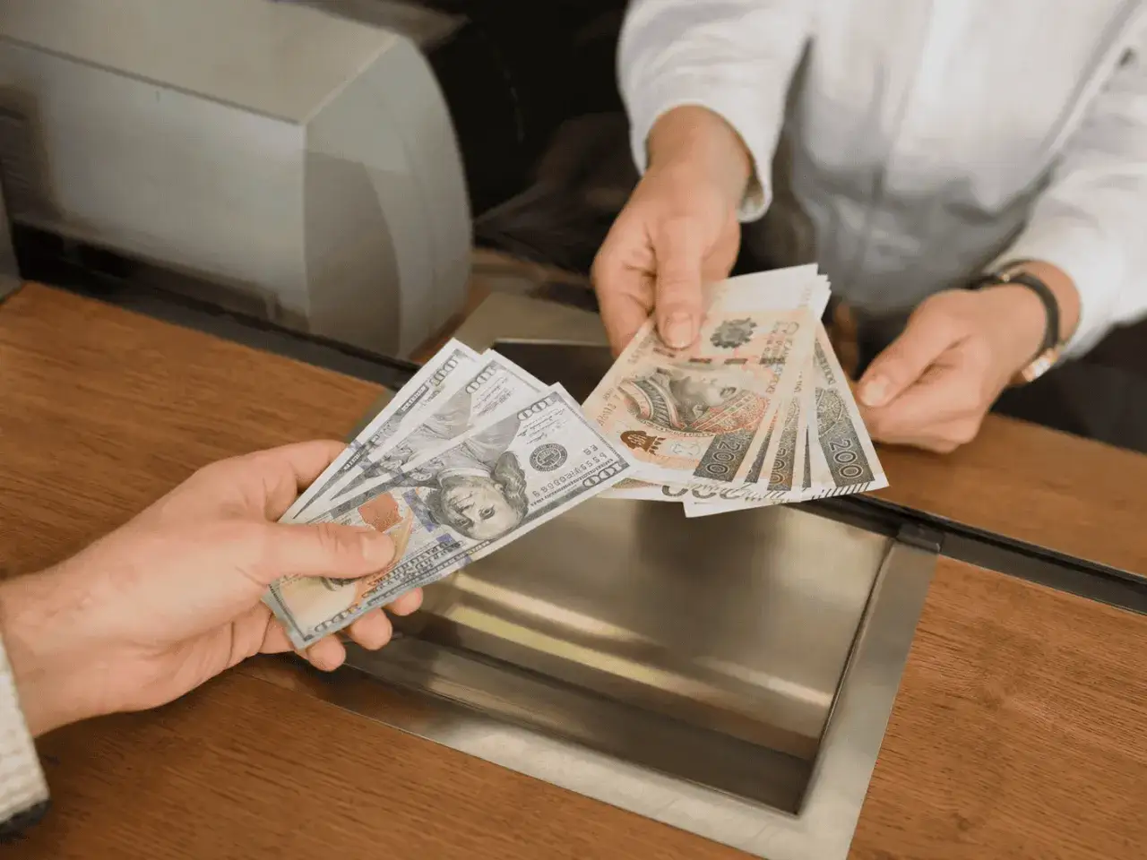 Dłonie wymieniają banknoty 100 dolar&oacute;w na polskie 200 zł. Czy warto kupować dolary? Decyzja zależy od kursu.