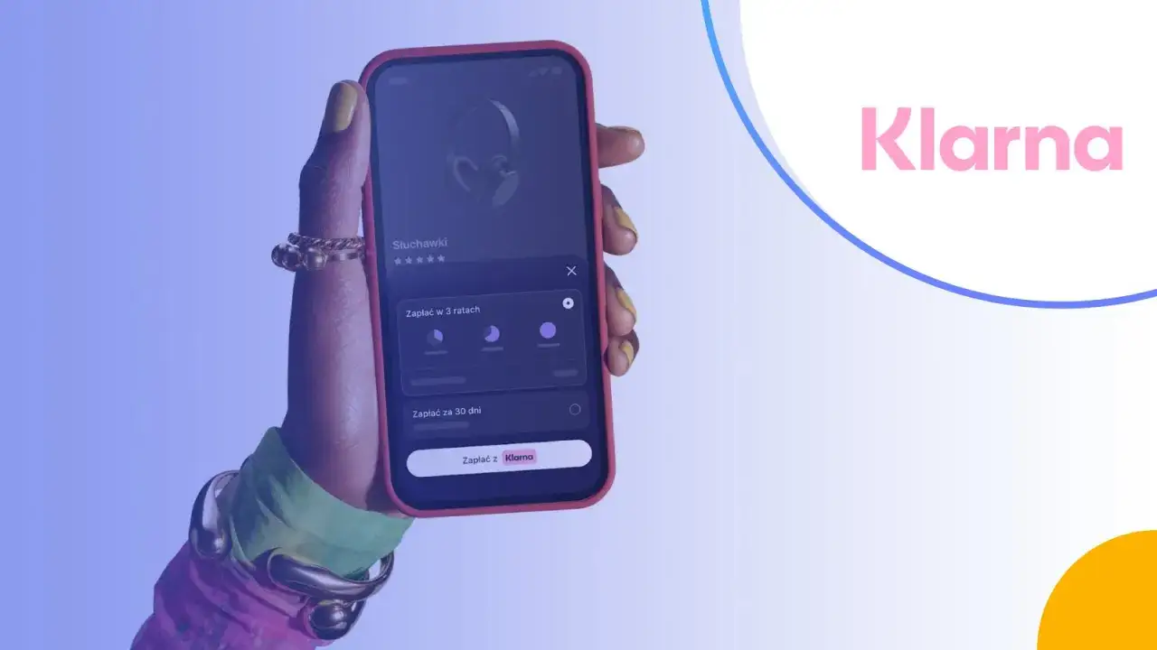 Dłoń trzyma telefon z aplikacją Klarna, pokazującą opcje płatności za słuchawki. Czy Klarna jest bezpieczna? Tak, to popularny spos&oacute;b na zakupy.