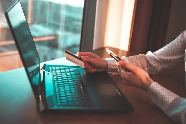 Osoba z kartą płatniczą i telefonem przy laptopie, szuka informacji jak cofnąć przelew Santander.